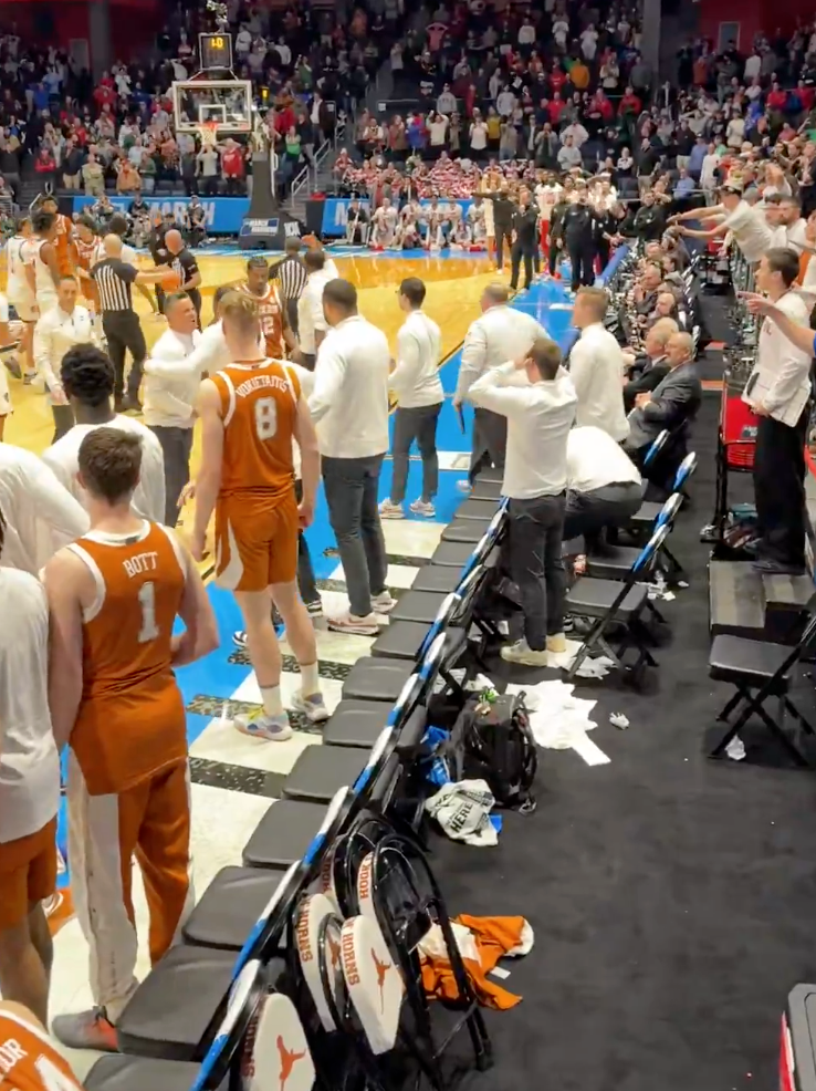 Basketball game with players, coaches, and staff on the court and fans in the stands.